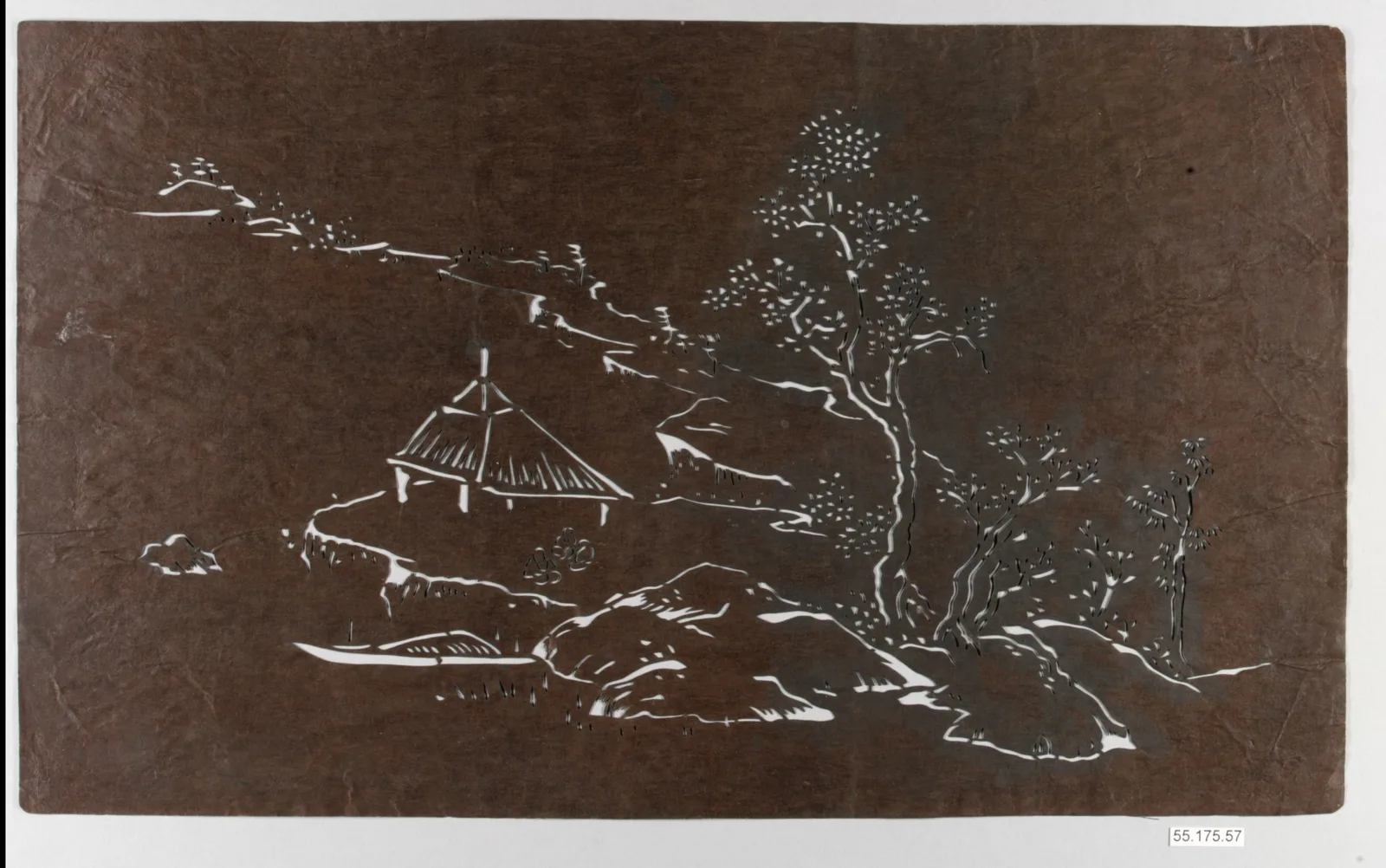 A carved paper dye stencil with a landscape of a hut and pines