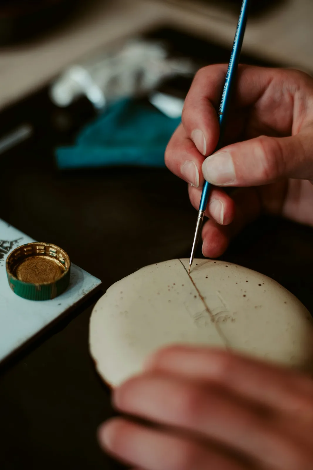 A hand paints a detail on a ceramic piece