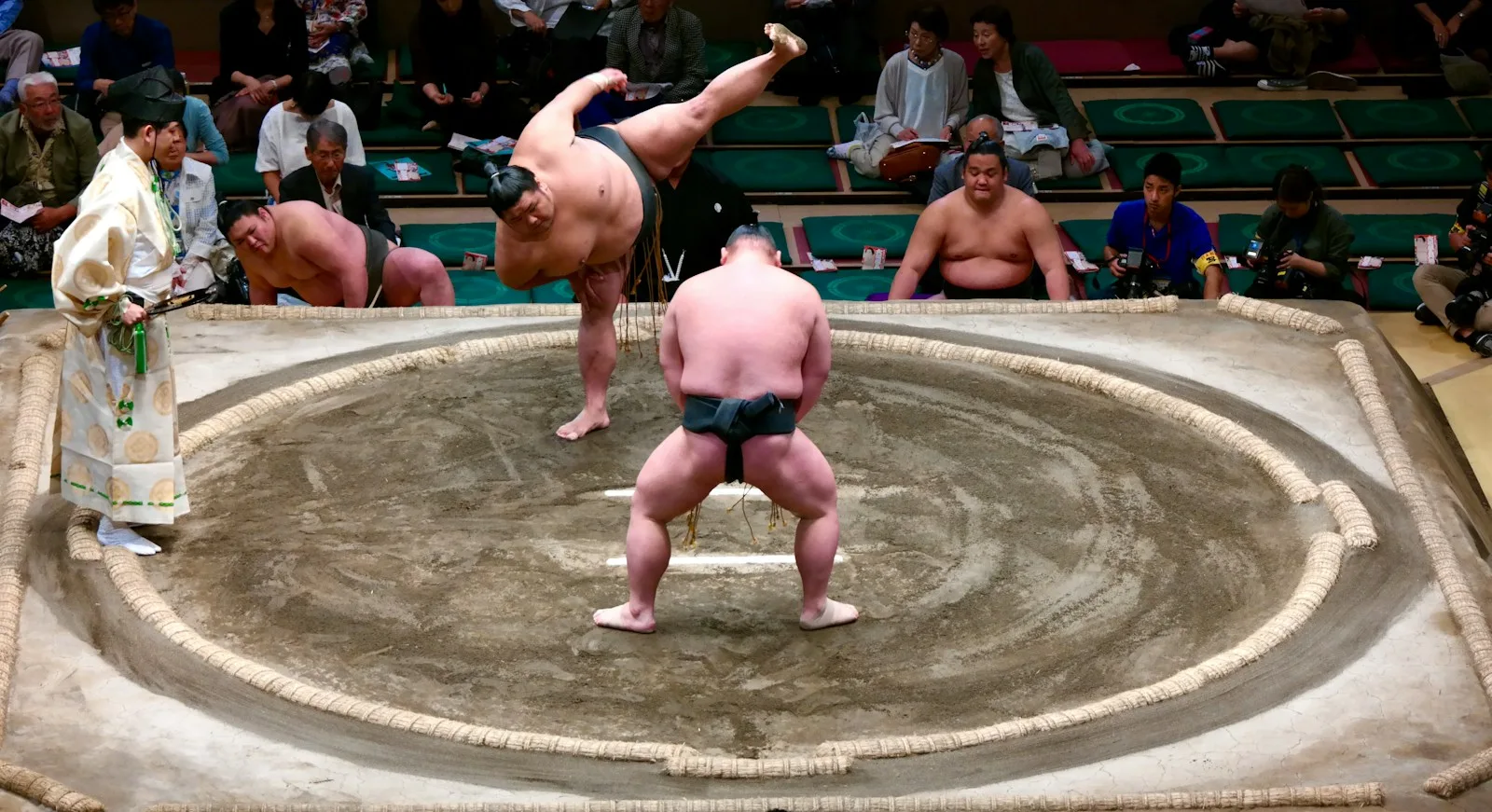 Sumo wrestlers mid-bout in the ring, watched by the referee