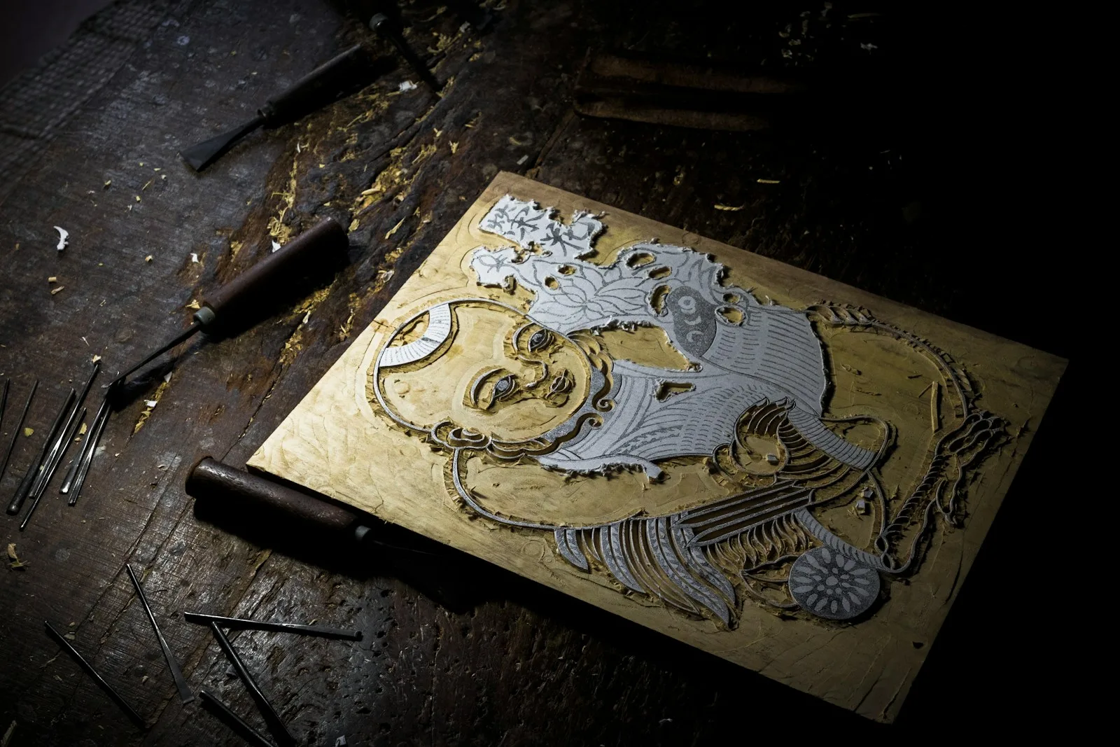 A carved woodblock and tools on a printmaker's workbench