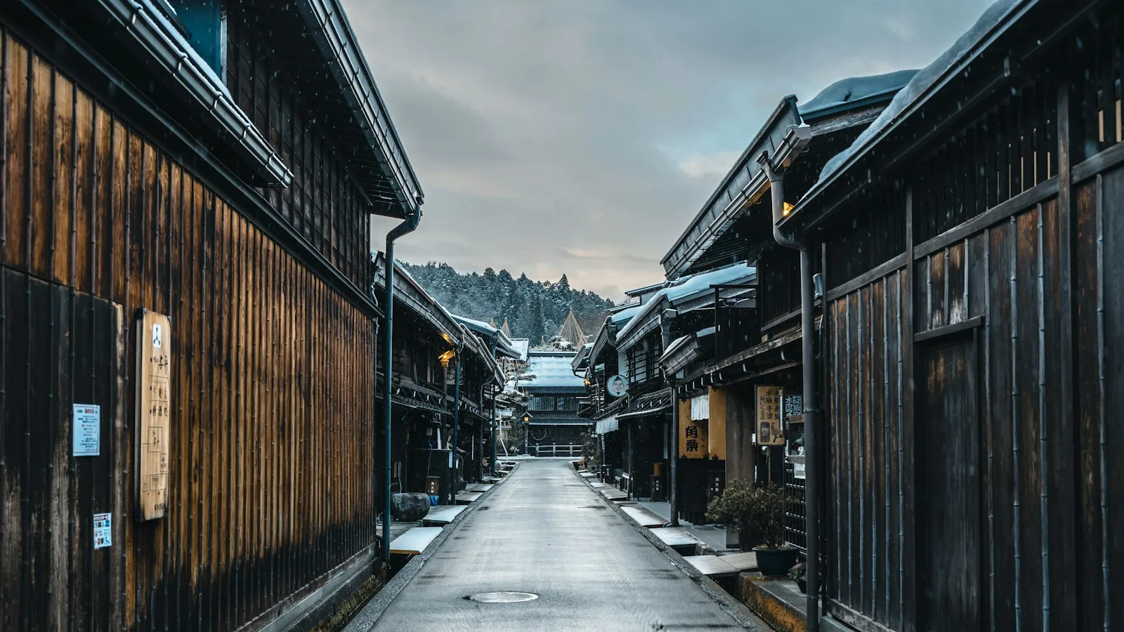 A narrow street with wooden buildings and snow on the ground